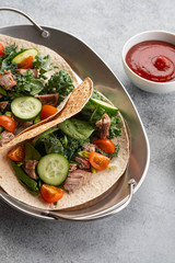 Two mexican pork carnitas tacos with sauces and vegetables.