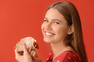 Woman eating tasty taco on color background