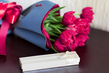 Designed bouquet of fresh brigh pink tulips with a gift box on light green background with copy space for any text or message.