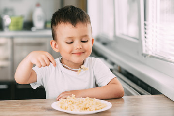 a child in the kitchen during the day eating pasta in a spiral in a white t-shirt
