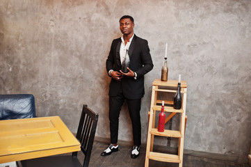 Strong powerful african american man in black suit posed against gray wall with candle decorations.
