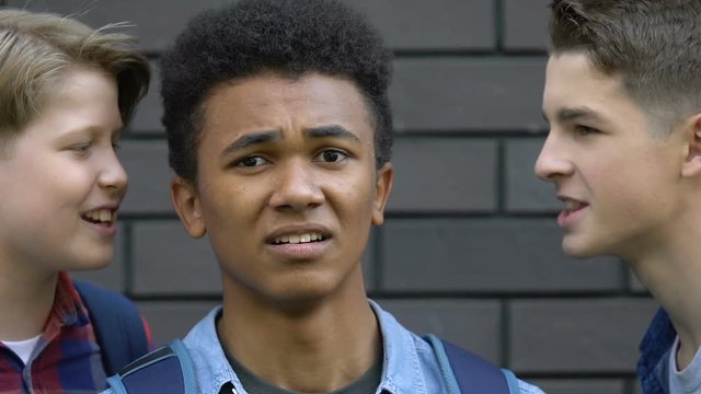 Rude teenagers mocking stressed afro-american guy looking in despair to cam