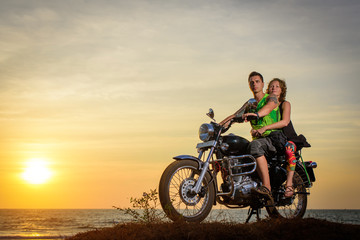 Obraz na płótnie Canvas Romantic picture with a couple of beautiful stylish bikers at sunset. Handsome guy with tatoo and young sexy woman enjoy themselves in motorbike trip.