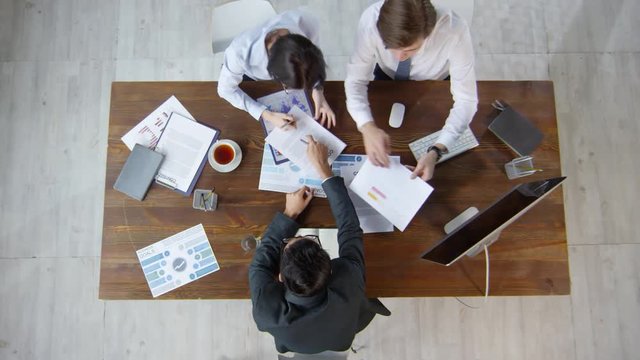 Directly above shot of businesswoman and businessmen sitting at table and working with various documents, then making notes in planners