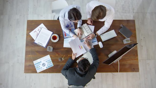 Top view shot with timelapse of businesspeople sitting at table and working with documents during meeting with business consultant