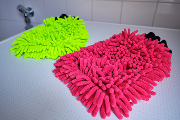 A neon yellow and a red wash mitt lying on white background in the bathroom