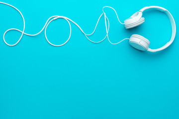 White headphones with cable. Top view of headphones on turquoise blue background. Minimalist photo...