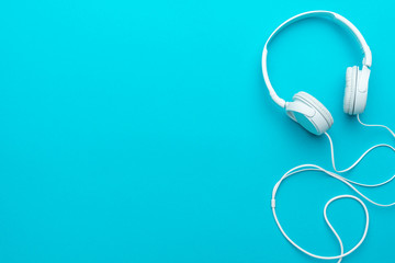 White headphones with cable. Top view of headphones on turquoise blue background. Minimalist photo...