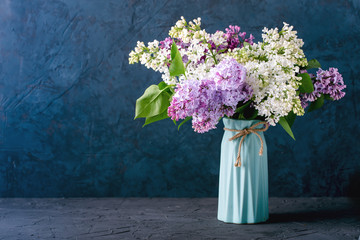Bouquet of colorful lilacs, in ceramic blue vase, on table, on darck blue gray background, place...