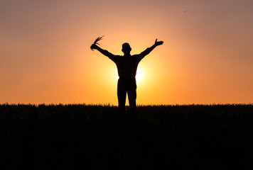 Silhouette of senior farmer standing in field with his hands outstretched.