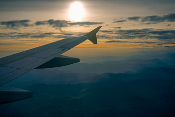 Fototapeta premium Lowkey image of airplane wing in the sky over mountains. Spectacular view of a sunset above the mountains. Aerial shot from airplane window.