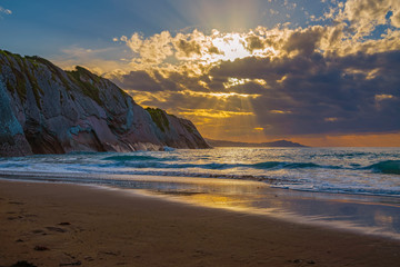 Gorgeous seascape. Beautiful sunset reflected in the waves. Silhouettes of mountains on the horizon. Itzurun beach, flysch of Zumaia on the coast of Gipuzkoa, Spain. Low key, natural dark background.