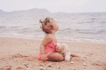 pensive little girl hugging teddy bear and looking away while sitting on seashore.