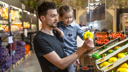 Happy family buys vegetables. Cheerful family of three choosing tomatoes in vegetable department of supermarket or market.