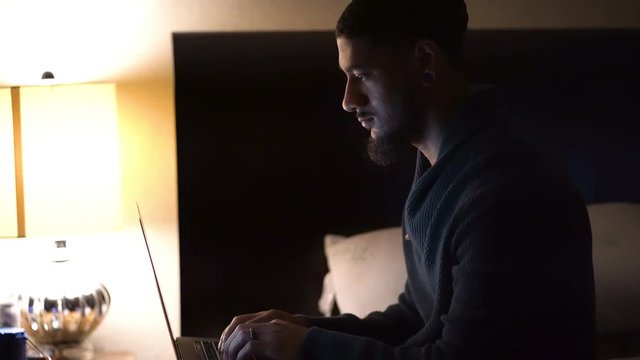Man typing on computer in his bedroom.