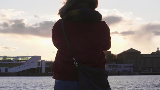 4K anamorphic video shot with gimbal of a young Norwegian woman taking photo of a beautiful sunset with her smartphone at the Soerenga pier, a popular tourist destination in Oslo, Norway.