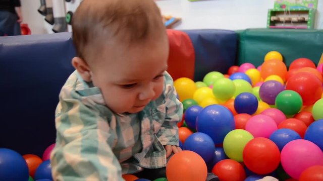 Cute six months old baby boy playing with colorful balls in children indoors playground