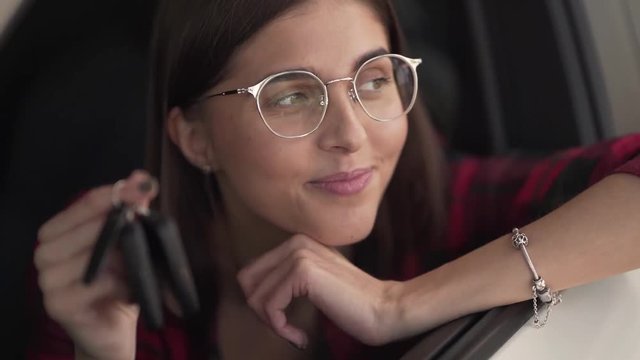 Close Up of Young Happy Caucasian Female Sitting In New White Car Leaning Her Head on Window and Holding Keys Recieved After Signing Leasing. Non Recognizable Vehicle Brand and Model