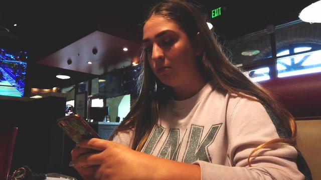 Static shot, of teenage female on phone, in restaurant, looking at social media and texting, at lunch, in California, USA