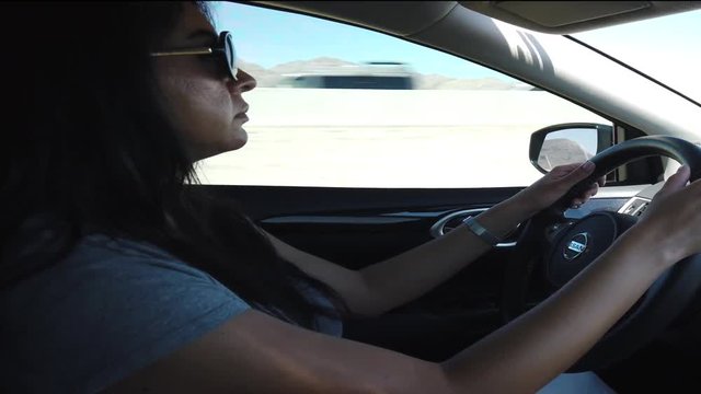 Static, shot of a woman wearing sunglasses and driving a Nissan car, in Los Angeles, California, USA