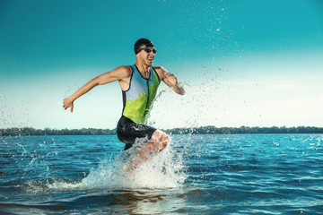 Professional triathlete swimming in river's open water. Man wearing swim equipment practicing triathlon on the beach in summer's day. Concept of healthy lifestyle, sport, action, motion and movement. - obrazy, fototapety, plakaty