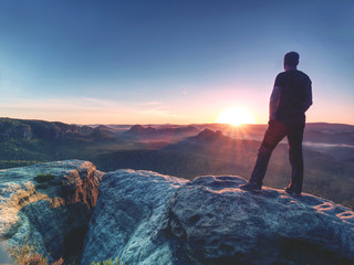 Man hiker at mountain peak. Nice daybreak in misty landscape.