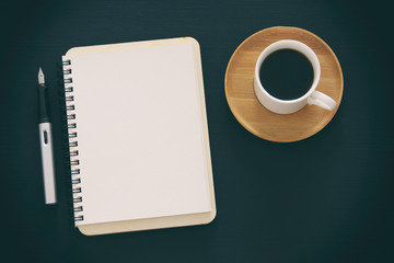 Open notebook with empty pages and other office supplies over black office desk table. Top view