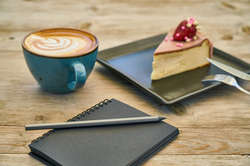 Latte coffee, cheesecake and notebook on the table