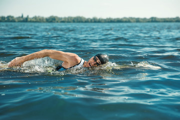 Professional triathlete swimming in river's open water. Man wearing swim equipment practicing triathlon on the beach in summer's day. Concept of healthy lifestyle, sport, action, motion and movement.