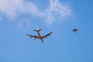 Military tanker aircraft (refueler) and fighter jet fly on blue sky and clouds background