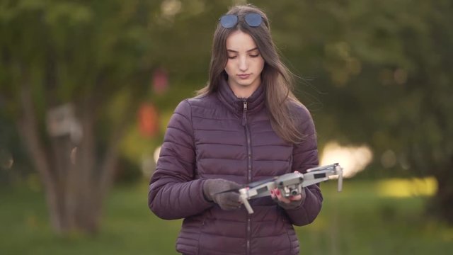 Young Caucasian Female Releasing Propellers on Small Drone Before Flight in Green Park. Blurred Background