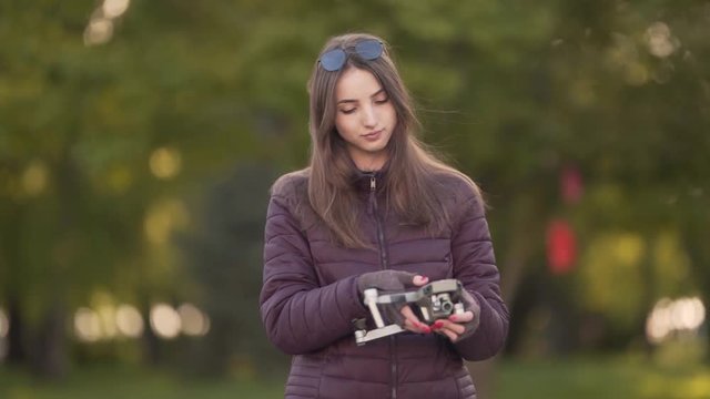Young Caucasian Female With Gloves on Hands Releasing Landing Gear and Propellers on Small Drone Before Flight. Blurred Background