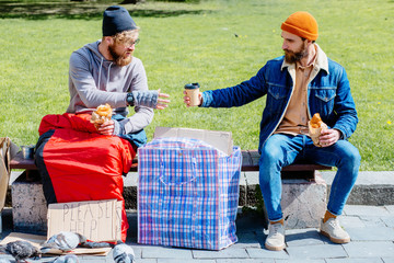 Sympathetic beard hipster man giving his breakfast- coffee and croissant while helpless hungry...