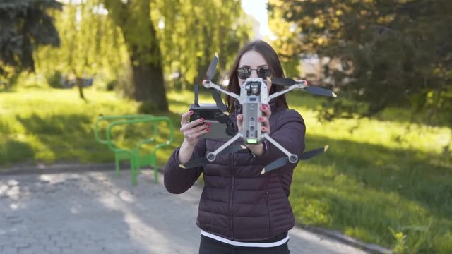 Beautiful girl in a sunglasses is operating a drone and managing the height on which it is going up to have a great photos.