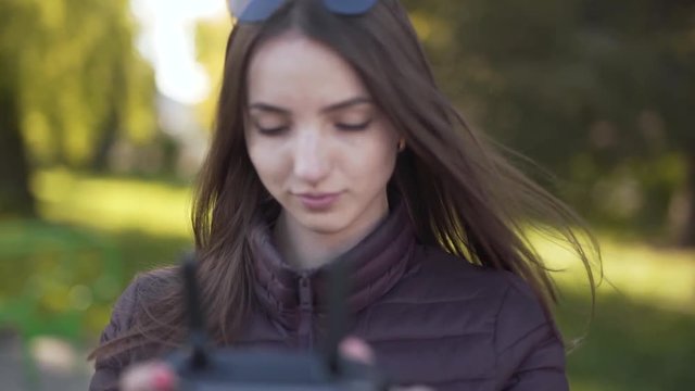 Beautiful girl in a sunglasses is operating a drone and managing the height on which it is going up to have a great photos.