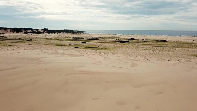 Cinematic Drone Aerial of Young Lonely Man Standing on Top of Sand Dune on Deserted Beach and Looking At Sea and Skyline on Horizon 4k
