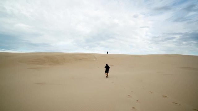 Cinematic Shot of Young Male Hiking in Desert Sand Over Dunes With Backpack Under Beautiful Australian Skyline. Camera Back Follow Movement 4k