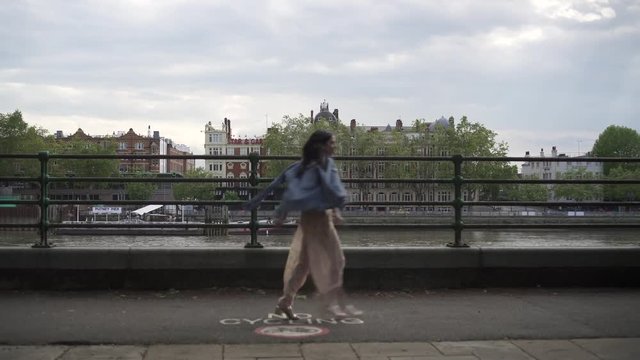 Fashionable latina tourist with black wavy hair and a jean jacket walking and spinning in London with a view of boats and buildings behind her