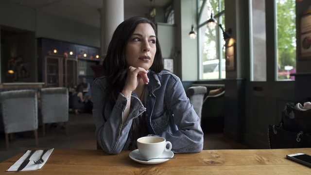 Beautiful Hispanic latina brunette sitting at the table waiting while having a coffee