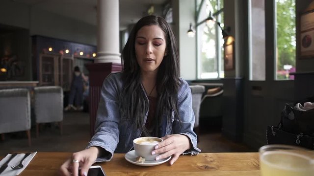 Attractive hispanic brunette sitting at the table, having a coffee while checking her phone
