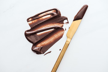 Top view of gold table knife with liquid chocolate on white background