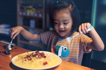 Asian little girl is eating spaghetti bolognese in the restaurant happily.