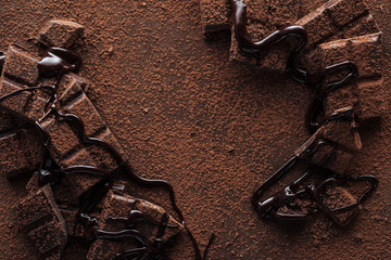 Top view of pieces of chocolate with liquid chocolate and cocoa powder on metal background