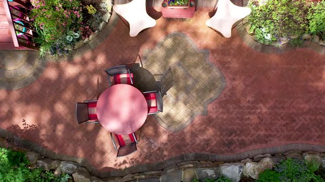 Aerial view ascending from herringbone brickscape showing completed hardscaping patio area with rock wall gardens melting into forest.