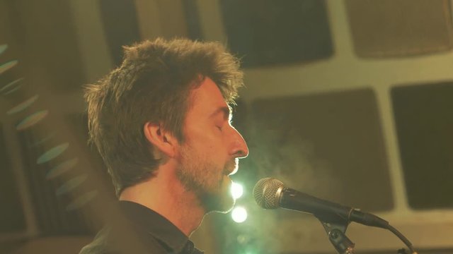 Musician on stage singing into mic eyes closed.