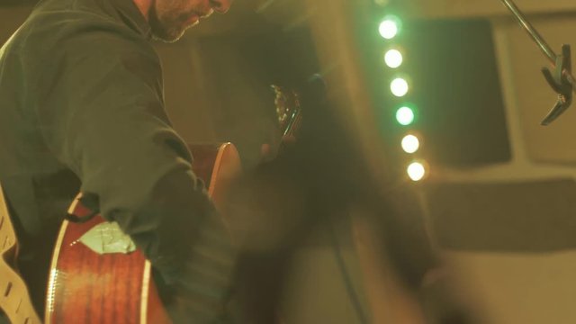 Musician plays acoustic guitar on stage singing into microphone.