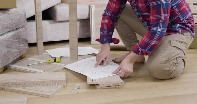 slow motion unrecognized male carpenter working with diy manual detail instruction paper on floor. surrounded with tools and wood. man with do it yourself furniture making house renovation process