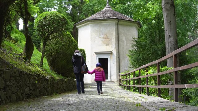 A mother and her little daughter carrying a teddy bear visiting the sacred mountain of Varallo christian devotional complex, a unesco world heritage site near the town of Varallo Sesia in Italy