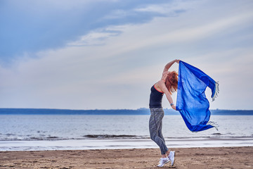 Slim red-haired middle-aged woman in sports form is engaged in dancing with a blue scarf. A woman...