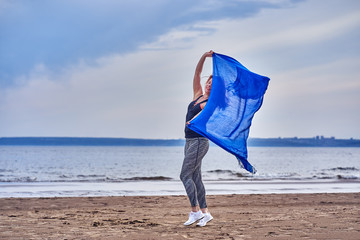 Slim red-haired middle-aged woman in sports form is engaged in dancing with a blue scarf. A woman...